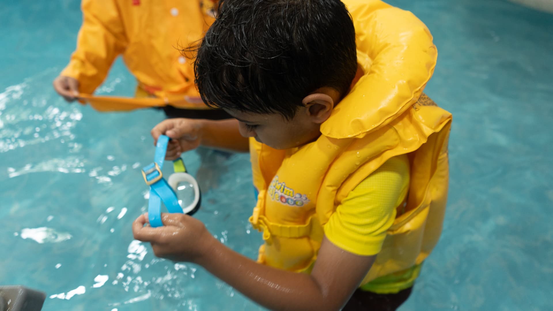 A child in a life jacket exploring the water with goggles in the aquatic room