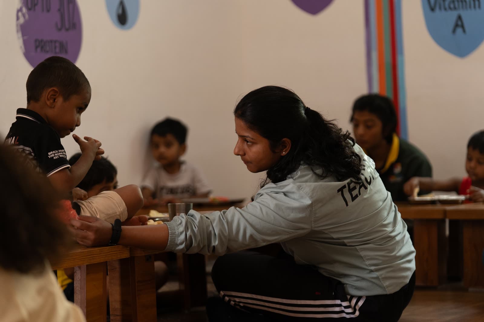 A mentor sitting with children during a meal at Athletots, Pashan