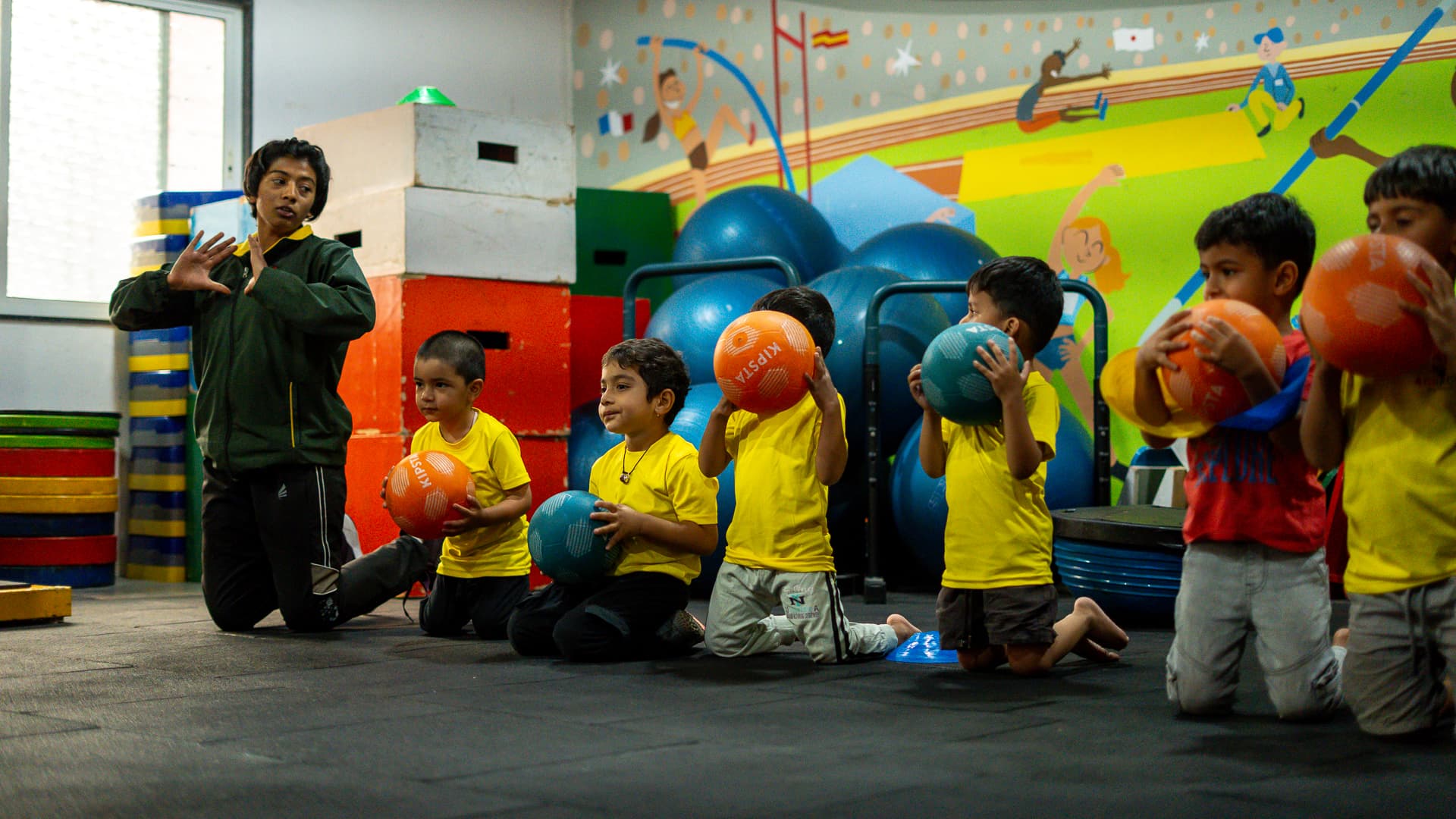 An Athletots coach briefing a Striders evening batch seated in a circle with training balls