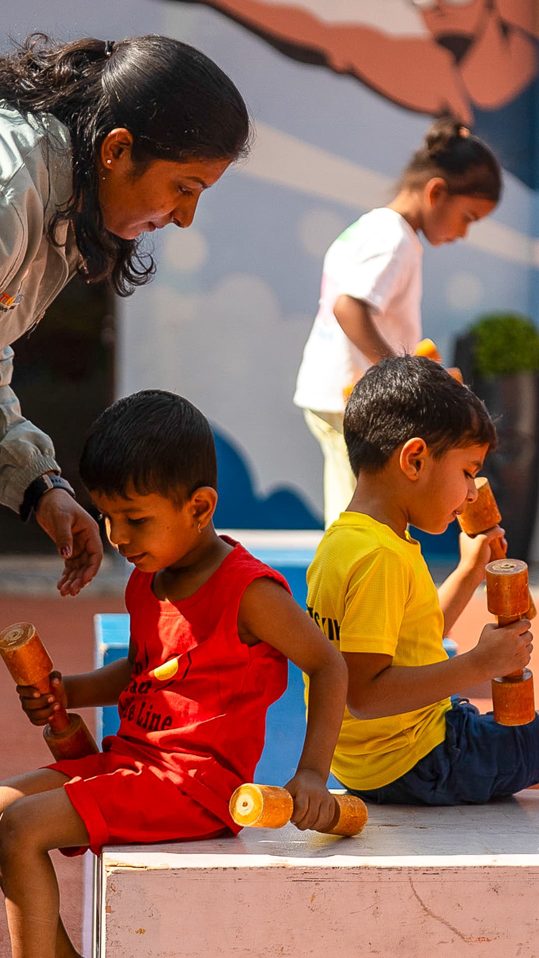 An Athletots mentor crouching beside two children holding relay batons before a session