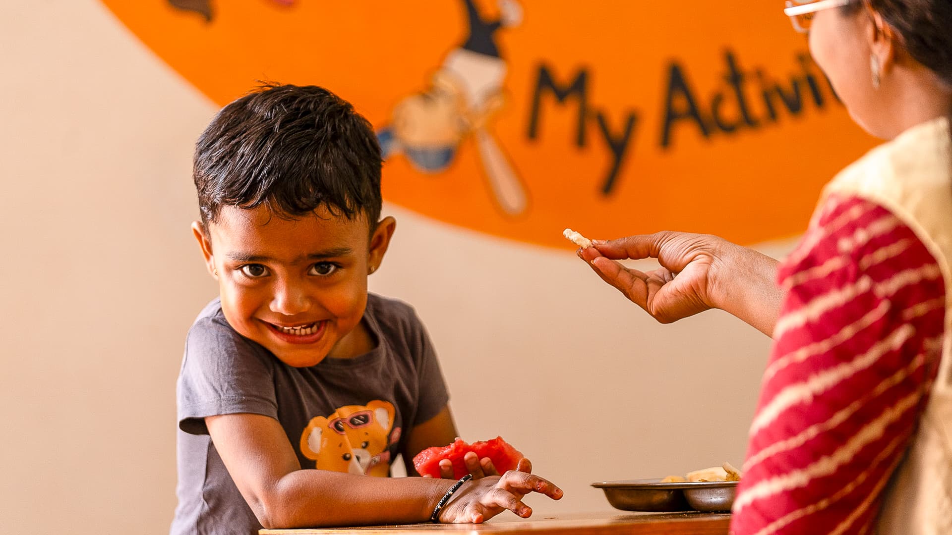 An Athletots mentor handing a child a piece of fruit at snack time